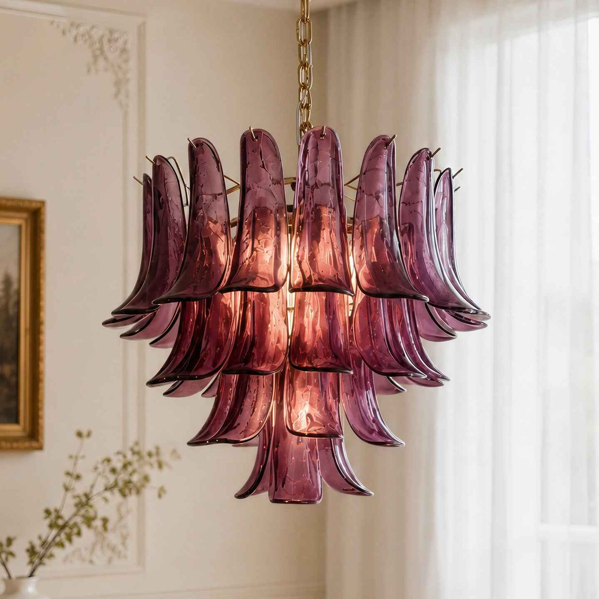 A modern chandelier with multiple layered, curved purple glass shades hanging from a gold chain in a bright, elegant room with white walls and sheer curtains.