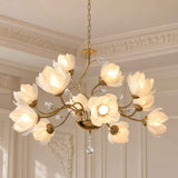A brass chandelier with 12 flower-shaped glass shades and hanging crystal prisms, shown lit in an elegant cream-colored room with decorative molding.