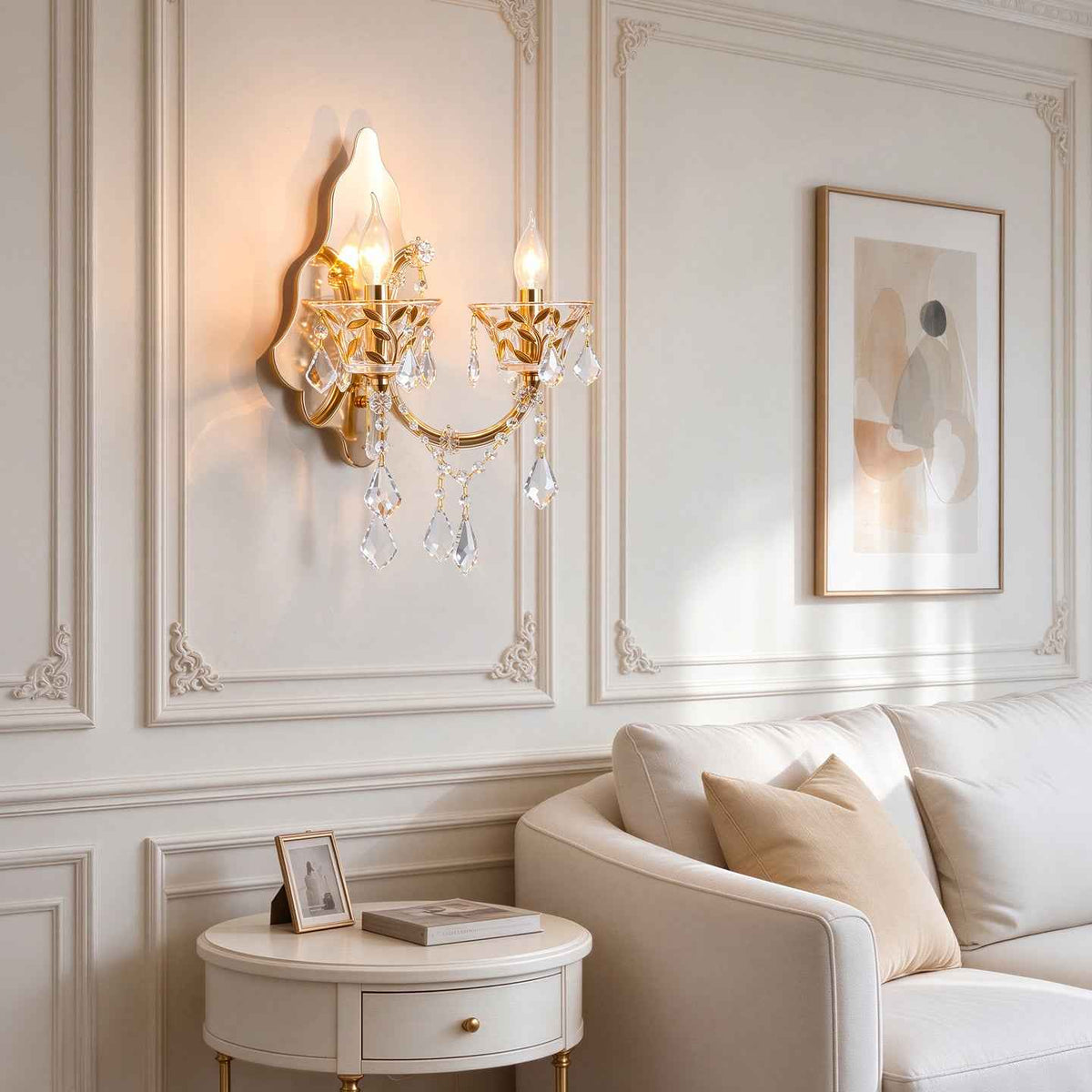 A gold wall sconce with hanging crystal prisms is mounted on a cream paneled wall above a white sofa in a styled living room.