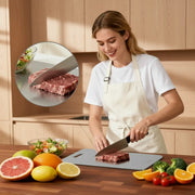 A woman in a white t-shirt and cream apron is shown slicing a raw steak on a gray cutting board in a kitchen setting. A circular inset highlights the steak being sliced.