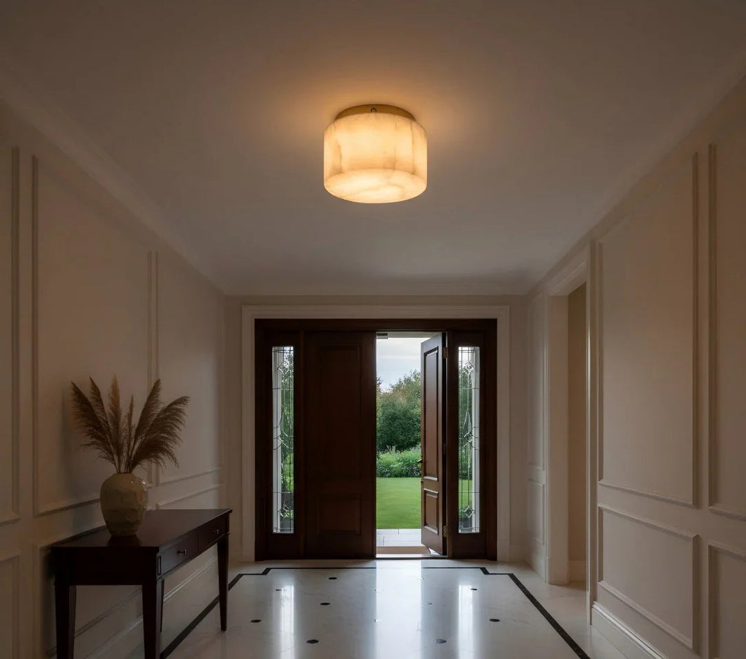 Cream alabaster flush mount light glows above a tiled foyer with an open wooden front door and console table.