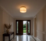 Cream alabaster flush mount light glows above a tiled foyer with an open wooden front door and console table.