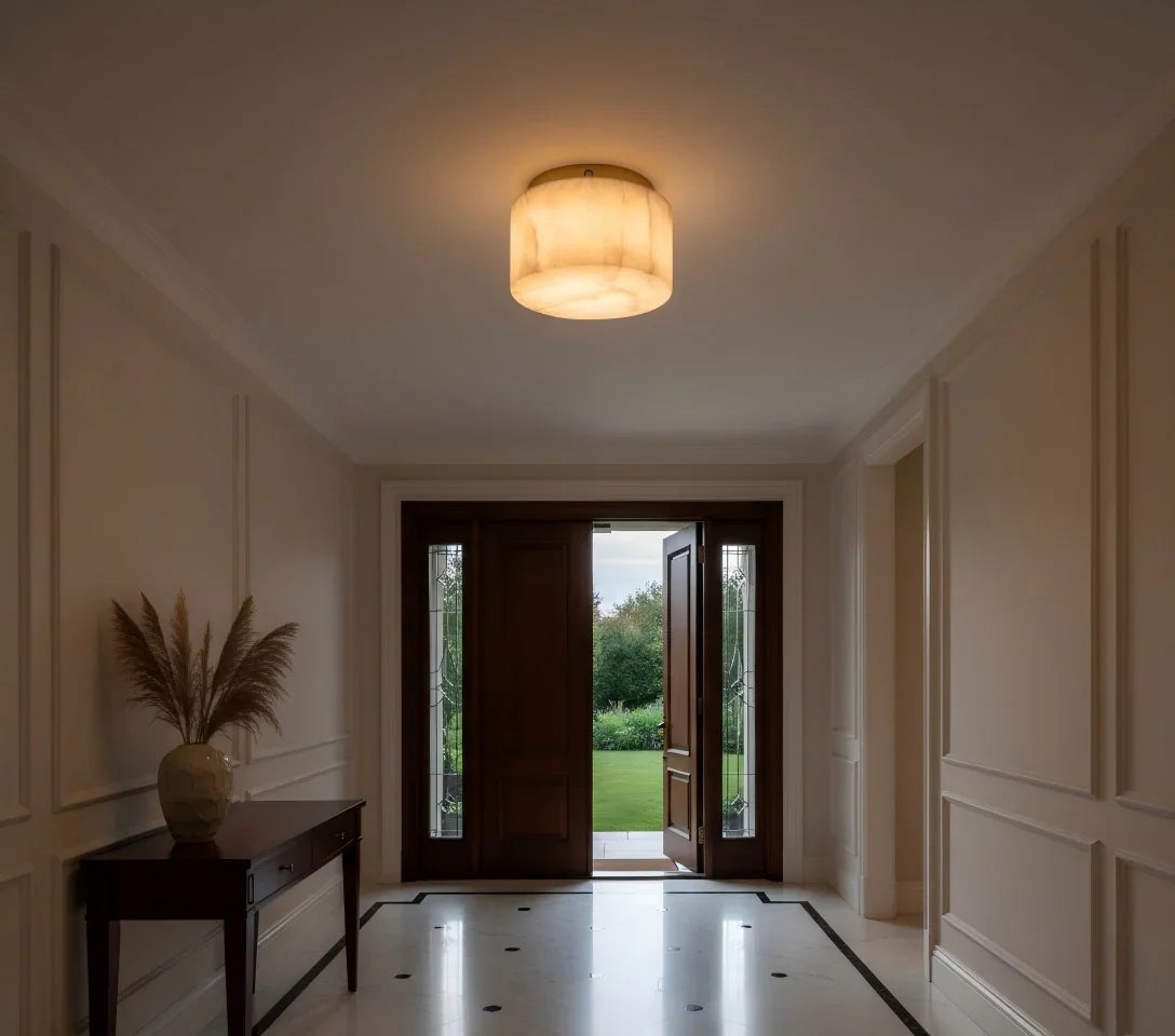 Cream alabaster flush mount light glows above a tiled foyer with an open wooden front door and console table.