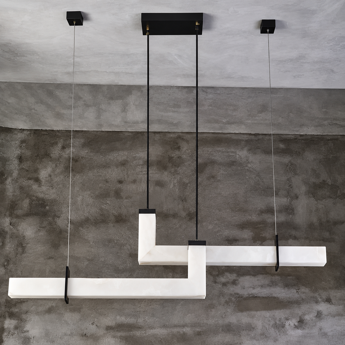 Modern geometric linear pendant light fixture with white marble-like horizontal bars suspended by black cables against a textured concrete wall and ceiling.