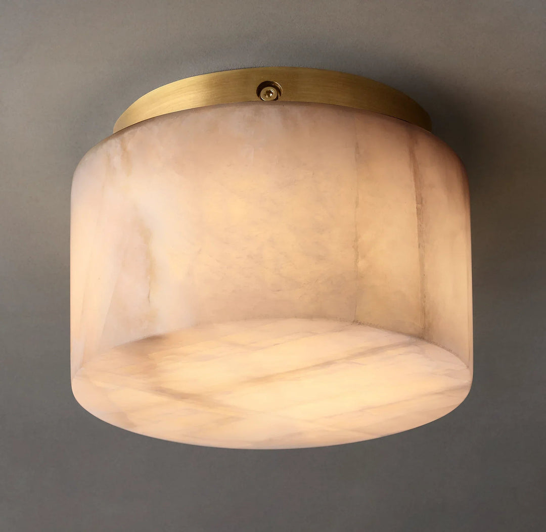 Illuminated alabaster drum flush mount light has cream veining and gold-colored ceiling trim against a gray background.