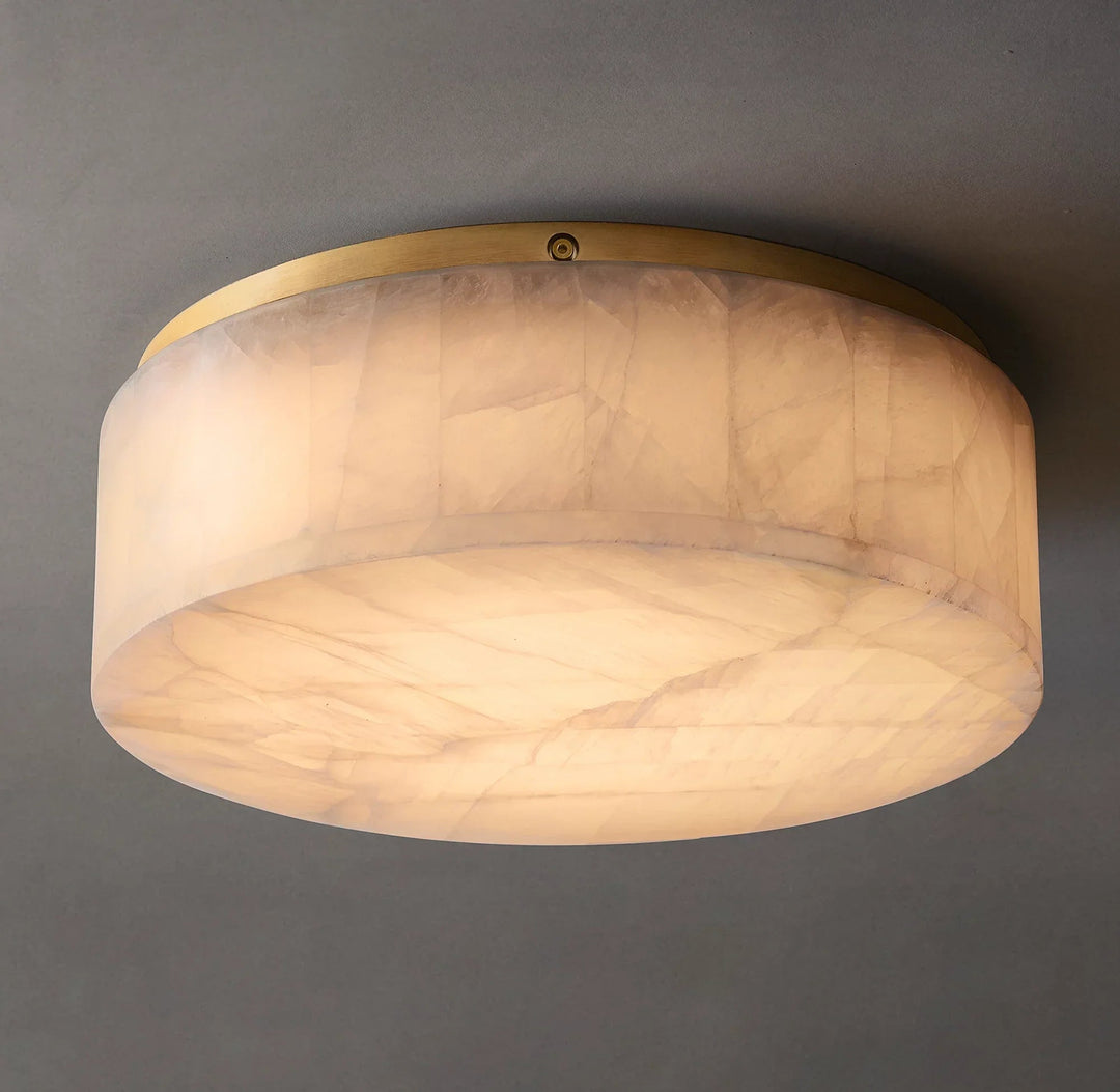 Low-angle view of an illuminated cream alabaster flush mount light with a gold-colored rim and broad circular underside against gray.