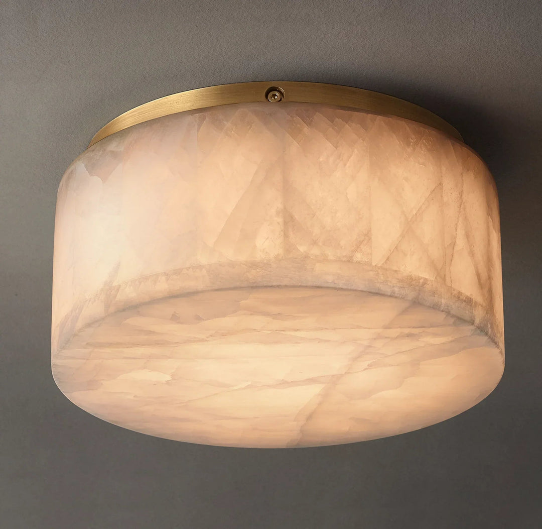 Alabaster drum flush mount light viewed from below, showing warm illumination, natural veining, and a gold-colored rim against gray.