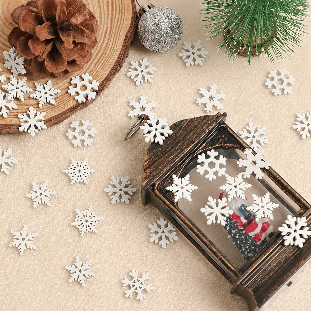 White wood snowflake ornaments surround a dark lantern on cream fabric beside a pinecone, wood slice, silver bauble, and miniature tree.