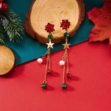 Red bow drop earrings with gold-tone stars and dangling bells rest beside wood slices on a red and teal background.