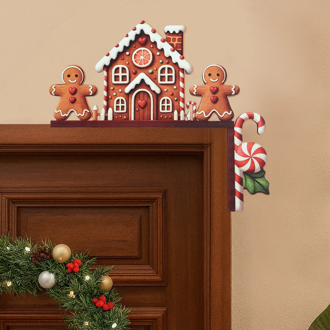 Gingerbread house door corner decoration with white icing details and two brown figures sits at a doorframe’s upper right corner above a wreath.