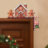 Gingerbread house door corner decoration with white icing details and two brown figures sits at a doorframe’s upper right corner above a wreath.