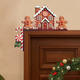 A gingerbread house corner decoration sits above a brown door, with a candy cane on the left and part of a wreath below.