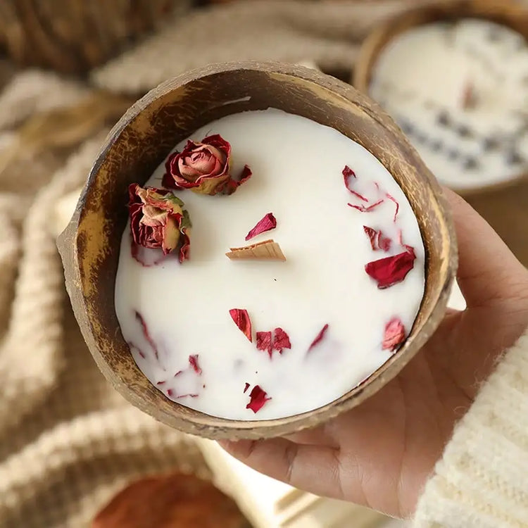 Hand holding a coconut shell candle topped with dried rose petals