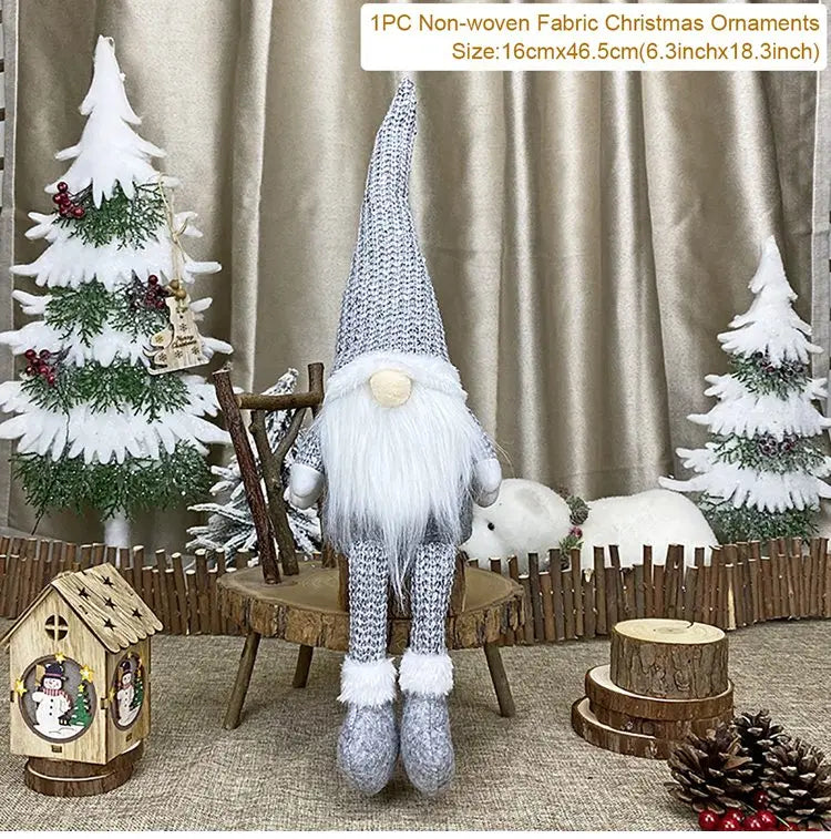 Gray gnome with dangling legs sits on a rustic chair among Christmas decorations, with a size label reading 16 × 46.5 cm.