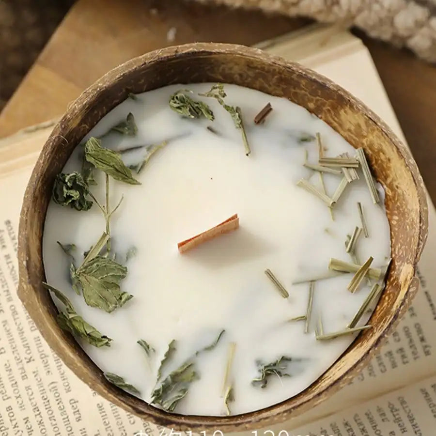 Coconut shell candle with dried mint and lemongrass resting on an open book