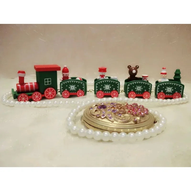 A green and red Christmas train decoration with snowflake details stands behind white beads and a gold floral ornament.