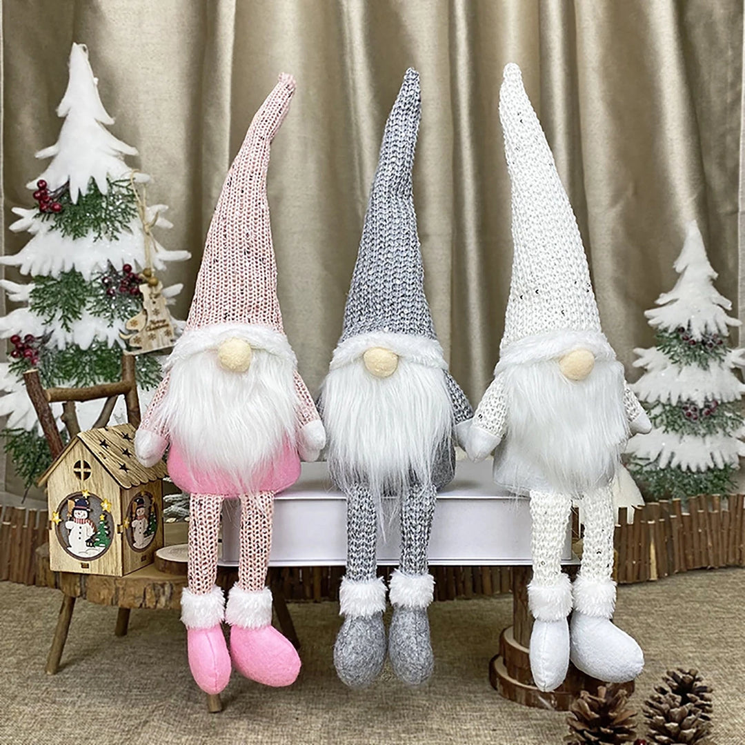 Pink, gray, and white gnomes with tall textured hats and dangling legs sit among miniature Christmas trees and pinecones.