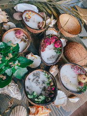Coconut shell candles with dried roses, lavender and eucalyptus beside seashells on driftwood