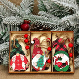 Red and green gnome Christmas ornaments with red-beaded hanging cords fill a three-compartment box beneath snowy evergreen branches.