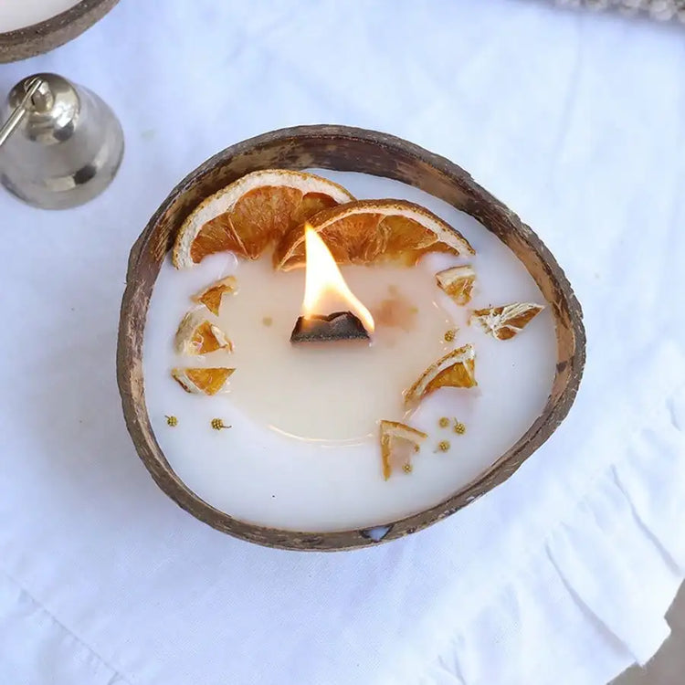 Coconut shell candle with dried orange slices, lit, on white fabric