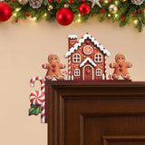 Gingerbread house door corner decoration with two brown figures and a striped candy cane sits on a dark doorframe beneath festive garland.