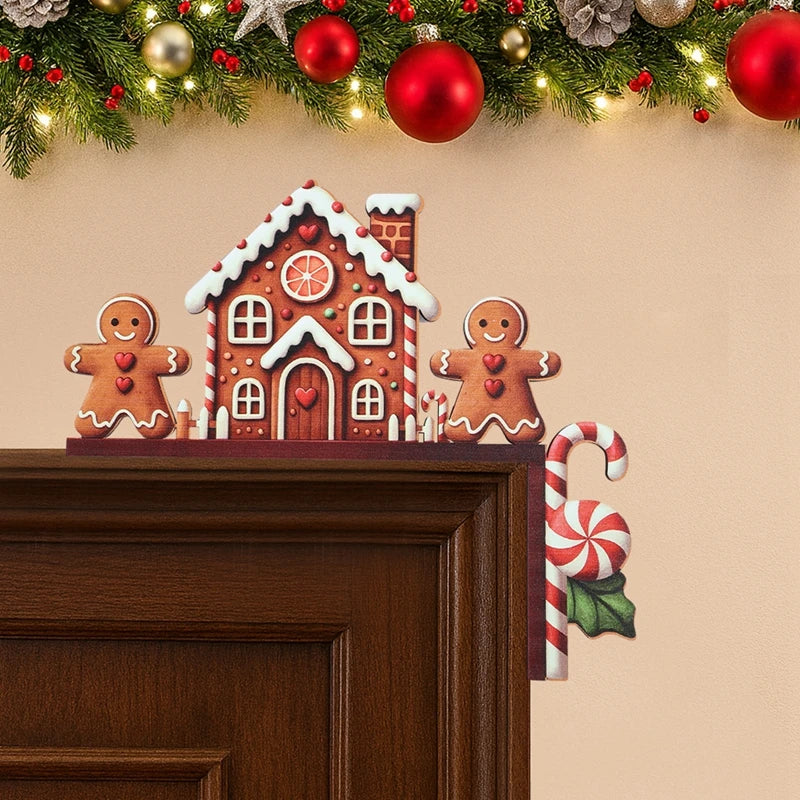 Brown gingerbread house door corner decoration sits on dark wooden door trim beneath garland decorated with red and gold baubles.