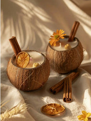 Two coconut shell candles with cinnamon sticks and dried orange slices in warm light