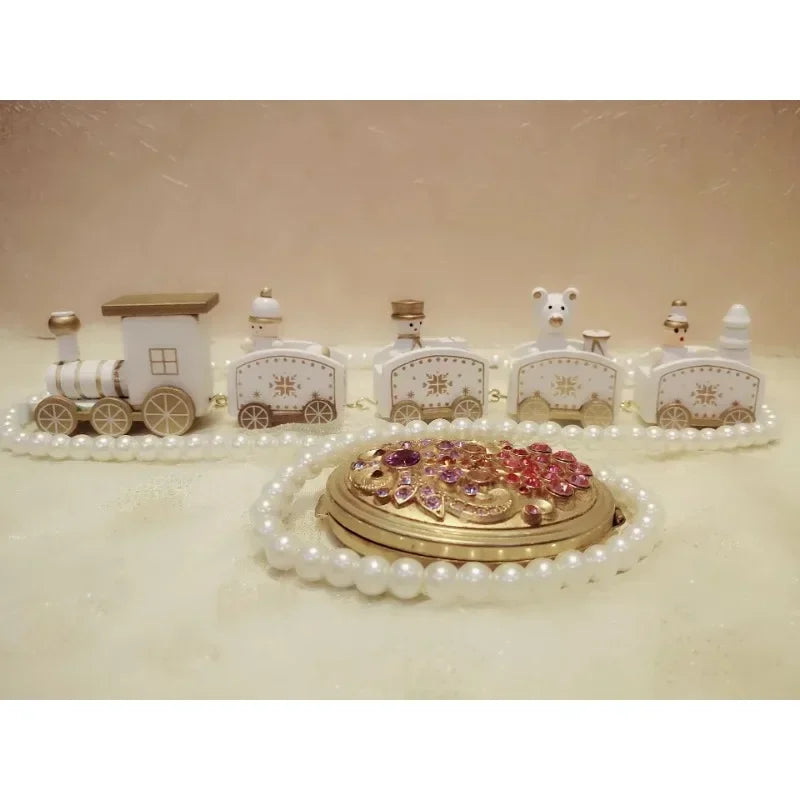 A white and gold Christmas train decoration with snowflake details stands behind white beads and a gold floral ornament.