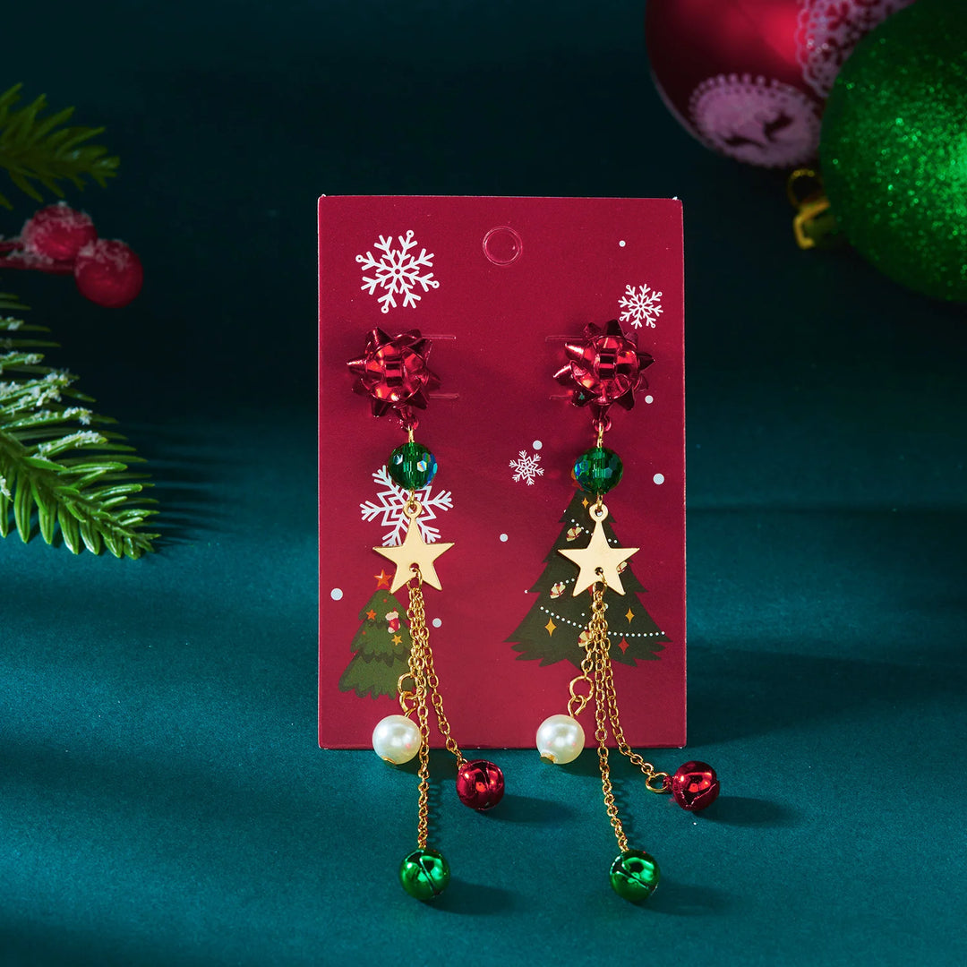 Red bow drop earrings with green beads, gold-tone stars, and bells hang on a red Christmas card against a teal background.