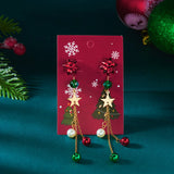 Red bow drop earrings with green beads, gold-tone stars, and bells hang on a red Christmas card against a teal background.