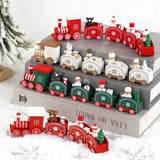 Red, green, and white Christmas train decorations sit on stacked books surrounded by faux snow beside a frosted tree.