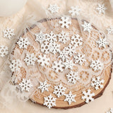 White wood snowflake ornaments in assorted designs lie scattered across cream lace draped over a round wood slice.
