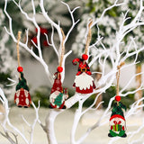 Four wooden gnome Christmas ornaments in red and green hang from white branches on cords with red beads.