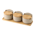 Three ceramic salt cellars with bamboo lids on a matching bamboo tray, top view