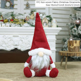 Red fabric Christmas gnome with a pointed hat and white beard sits before a decorated fireplace beside a 16 × 31 cm label.