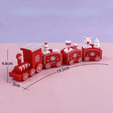 A red Christmas-themed toy train with three passenger cars and small festive decorations, shown on a pink surface with a lavender background. Black measurement lines and text indicate dimensions: 4.