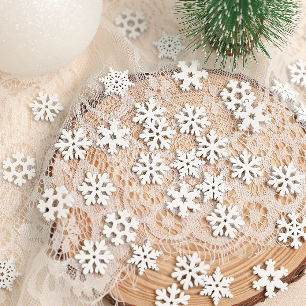 White wood snowflake ornaments cover lace over a round wood slice beside a miniature green tree and white bauble.