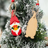 Two wooden gnome Christmas ornaments hang against snowy greenery, showing a red painted front holding a yellow gift and a plain back.