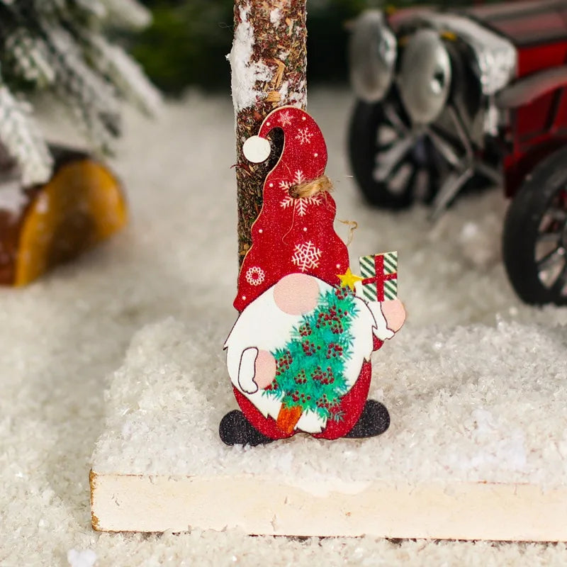 A red gnome ornament holding a green Christmas tree and striped gift rests against a snowy miniature tree trunk.