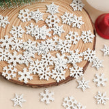 White wood snowflake ornaments in assorted patterns cover a round wood slice and cream fabric beside a red candle.