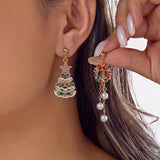 A model wears a green Christmas tree drop earring and holds a red and green wreath drop earring with three white beads.