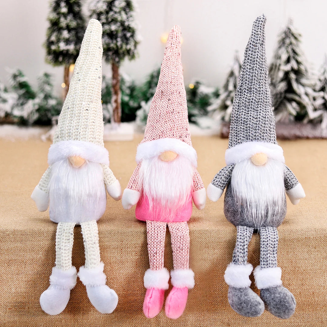 White, pink, and gray Christmas gnomes with pointed hats and white beards dangle their legs over a burlap-covered edge before miniature snowy trees.