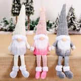 White, pink, and gray Christmas gnomes with pointed hats and white beards dangle their legs over a burlap-covered edge before miniature snowy trees.
