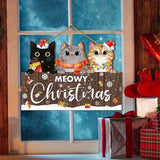 Brown Meowy Christmas hanging sign with three cats hangs against a blue window beside wrapped presents and red stockings.