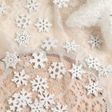 White wood snowflake ornaments rest on cream lace beside a partially visible glittery white star decoration.