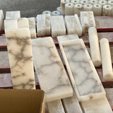 Pendant light alabaster material detail showing cream rectangular slabs and cylindrical stone pieces with gray veining on a wooden workbench.