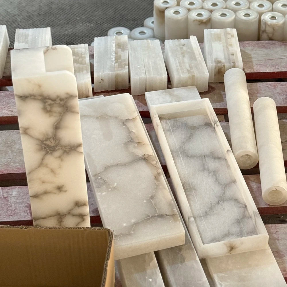Pendant light alabaster material detail showing cream rectangular slabs and cylindrical stone pieces with gray veining on a wooden workbench.