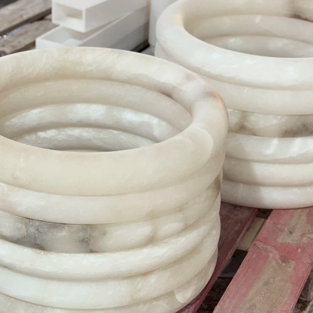 Creamy white alabaster pendant light components with natural veining are stacked in rings on wooden slats.