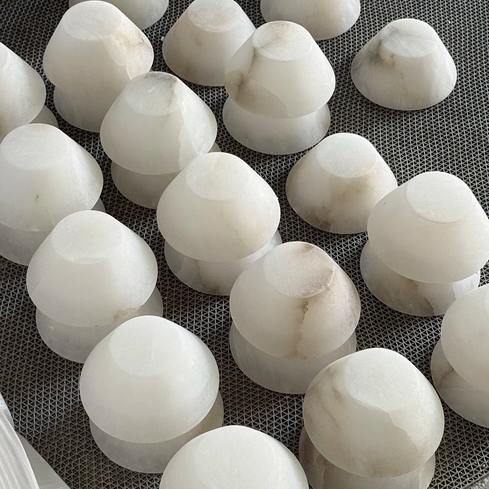 White alabaster pendant light shade components with natural veining are arranged on a dark mesh surface.