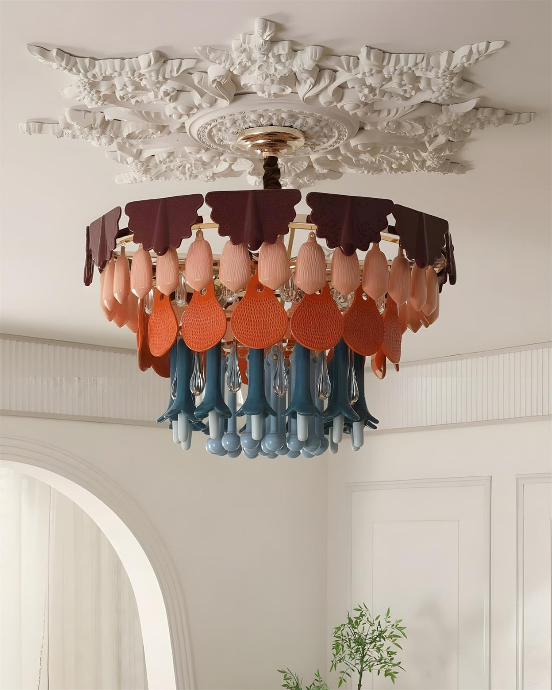Colorful chandelier hanging from a decorative ceiling in a room with white walls and a plant.